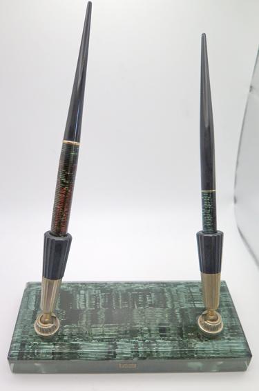 ITEM #4990: PARKER VACUMATIC DESK SET 7"x 3"x 3/4" THICK. GLASS/CELULLOID LAMINATED DESK BASE IN VACUMATIC GREEN. HOLDS 2 WRTITING INSTRUMENTS, FOUNTAIN PEN WITH BROAD/MED NIB + PENCIL. BOTH PEN & PENCIL WORK. SOCKETS ARE SIZED FOR EACH RESPECTIVELY. MATCHES GREEN LAMINTED PARKER VACUMATICS