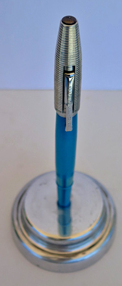 4585: REYNOLDS INTERNATIONAL BALLPOINT IN BRIGHT CHROME BLUE WITH ALUMINUM CAP WITH CIRCUMFERENTIAL GROVES. THE CAP REMOVES AND SNAPS ON OVER THE FRONT END OF THE PEN. COMES WITH PAPER INSTRUCTIONS AND GUARENTEE. CONTAINS AN ALUMINUM PEDISTOOL. ALL ITEMS FIT INSIDE AND ELABORATE DISPLAY CASE IN OLIVE GREEN WITH REYNOLDS PEN LOGO STILL VISABLE