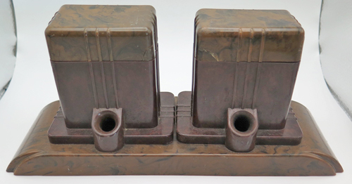ITEM #6663: FOUNT-O-INK BAKELITE DESK BASE IN BROWN TORTOISEHELL. HOLDS 2 PENS. HAS 2 ORIGINAL FOUNT-O-INK GLASS INK BOTTLES. ONE BOTTLE HAS CLASSIC FOUNT-O-PEN LABELS THAT WILL APEAR RIGHT SIDE UP WHEN IN USE. BOTTLES STILL CONTAINS BAKALIGHT VENT TUBES, ONE INTACT + ONE BROKEN IN 2 BUT FIXABLE. Lids that cover bottles (made of Bakelite) have tightly repaired cracks.